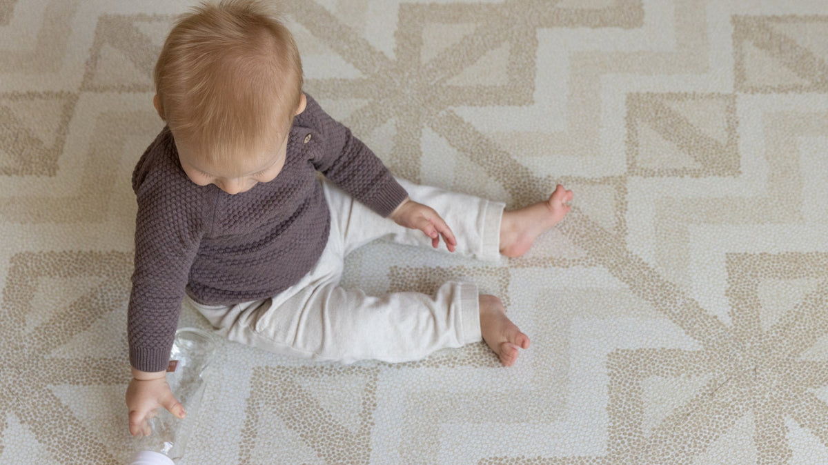 Kilim Sand speelmat met peuter die op de vloer speelt, het puzzelpatroon vult bijna de hele kamer